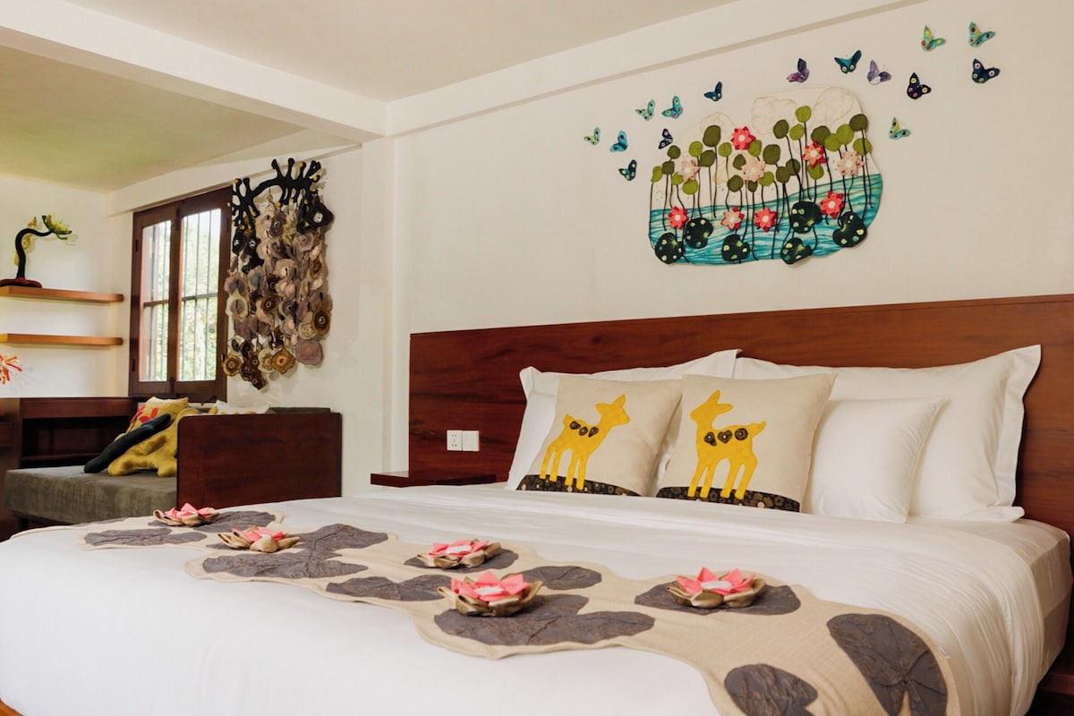 A neatly made bed with decorative pillows, a wall art piece with butterflies and flowers, and a wooden headboard.