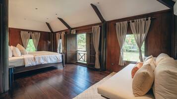A spacious bedroom with a large bed, a sofa, wooden flooring, and a view of greenery outside.