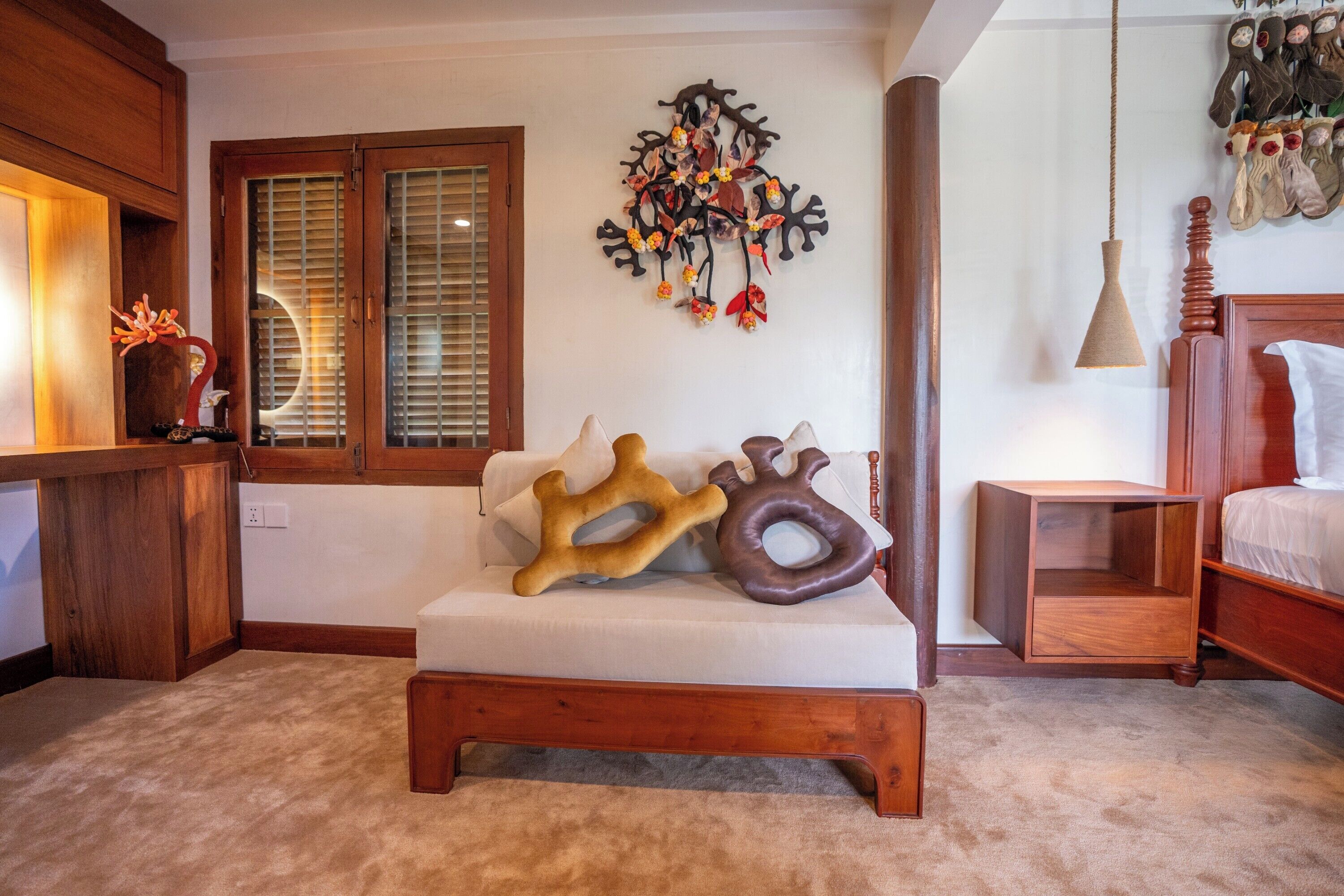 Une pièce comprenant un lit en bois, un canapé blanc, un élément décoratif mural et une table de chevet avec une lampe.