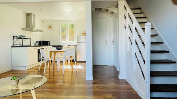 Una cucina moderna con mobili bianchi, una zona pranzo con tavolo in vetro e una scala che conduce a un altro piano.