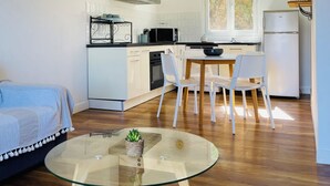 Una cucina moderna con mobili bianchi, una cappa in acciaio inossidabile e un frigorifero. È presente un'area pranzo con un tavolo in vetro e sedie.