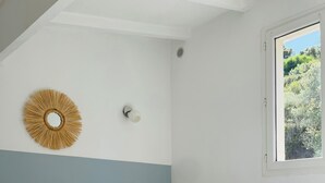 Una camera da letto con un letto, cuscini, una lampada a parete, una finestra vista sul verde e un elemento decorativo a parete.
