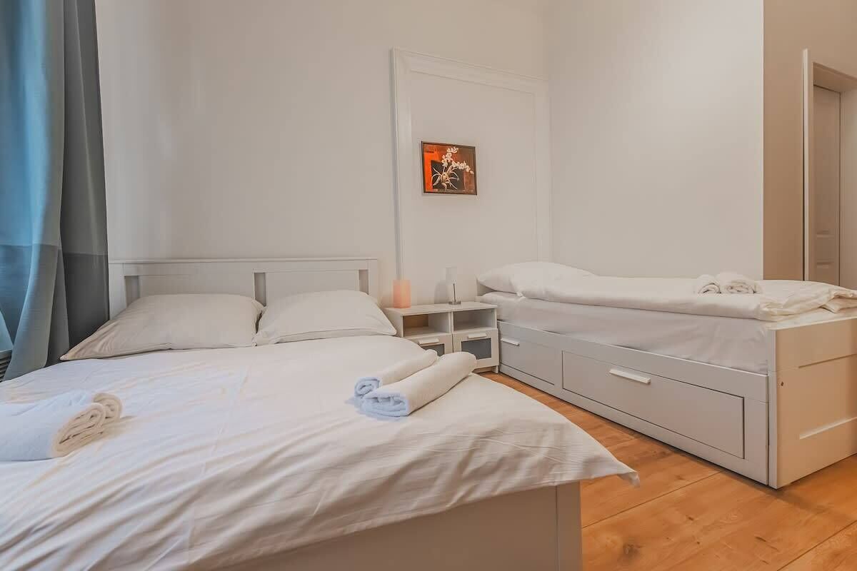 A bedroom with two beds, a bedside table, a nightstand, a wall-mounted artwork, and a door.