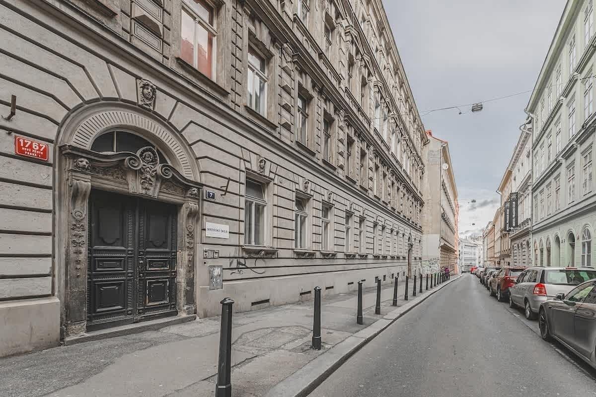 A street with historic buildings, a black metal fence, and parked cars.