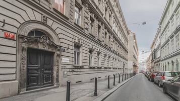 A street with historic buildings, a black metal fence, and parked cars.