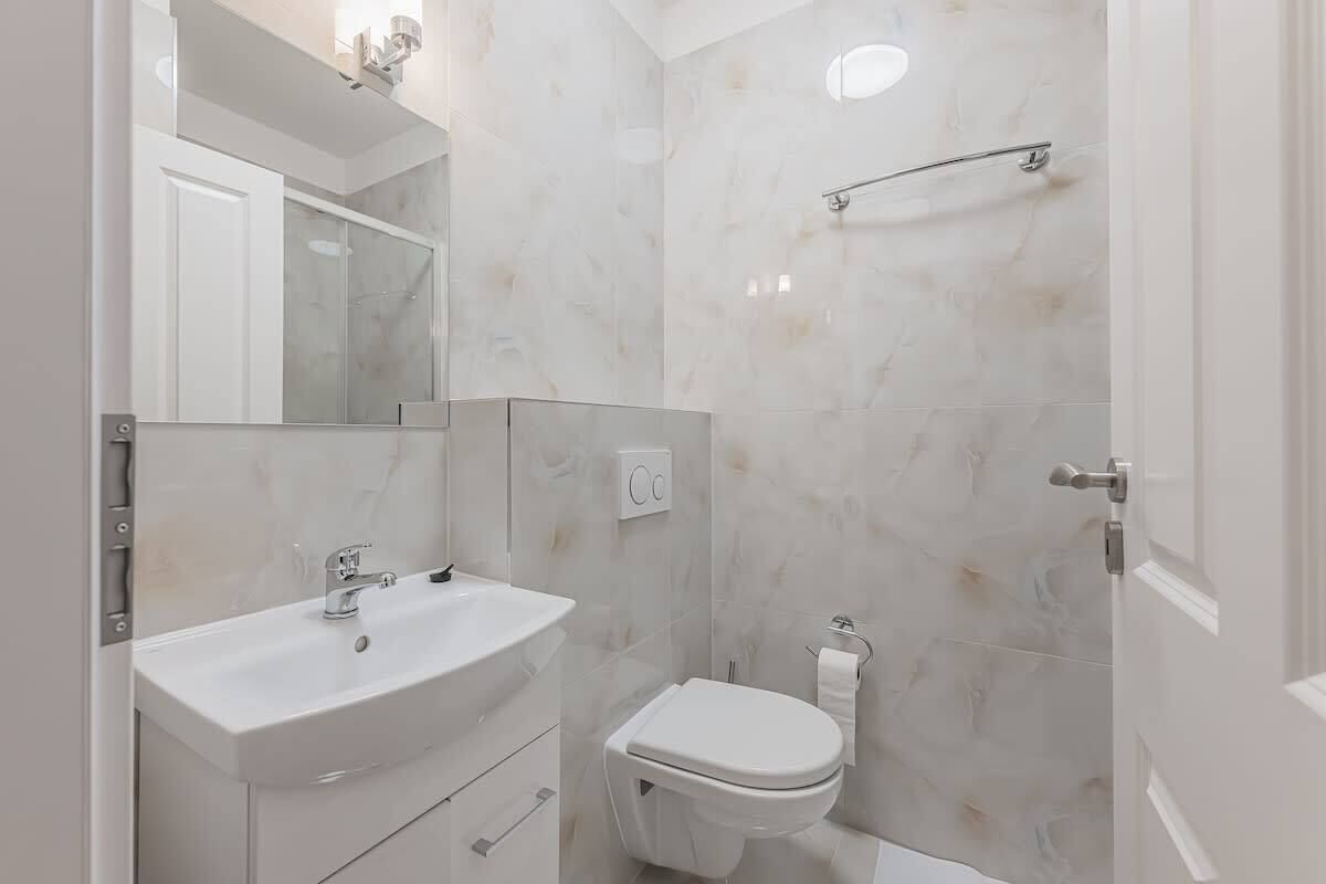 A bathroom with a white sink, mirror, and toilet, and a shower area with a glass door.