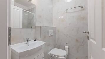 A bathroom with a white sink, mirror, and toilet, and a shower area with a glass door.
