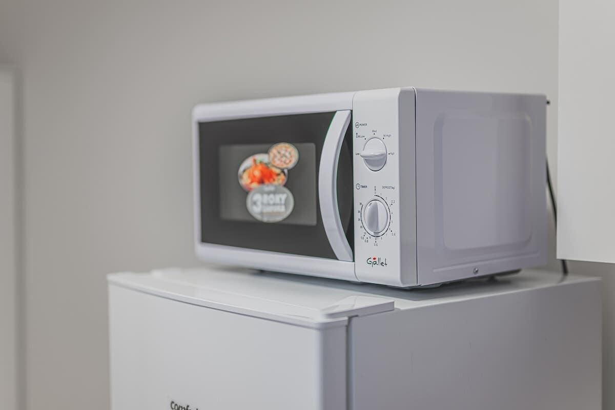 Un forno a microonde su un elettrodomestico bianco, forse un frigorifero, con un display digitale che mostra alimenti.
