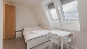 Et soveværelse med seng, skrivebord og et vindue med udsigt over bybilledet.