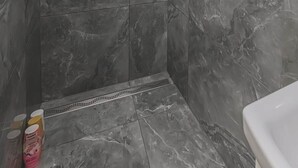 Een douche met een handdouche en een kraan op de muur, betegeld met een marmerachtige afwerking.