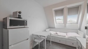 Pieni huone, jossa on sänky, pieni pöytä, mikroaaltouuni ja jääkaappi.