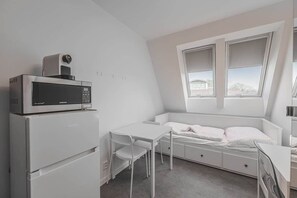 Ein kleines Zimmer mit einem Bett, einem Tisch, einer Mikrowelle und einem Kühlschrank.