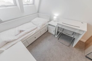 A small, white, single-bed room with a desk and chair, a bedside lamp, and a window. - Zizkov flat/skyline views/AC/Kitchen, new bathroom (Prague)