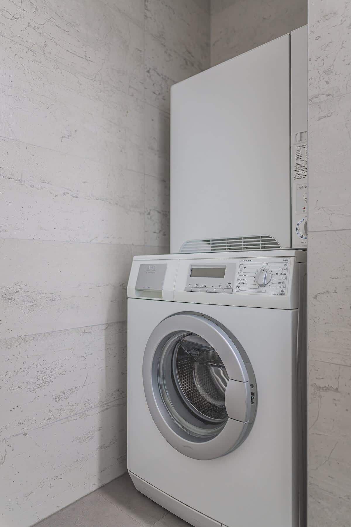 Une machine à laver à chargement frontal, placée dans un coin d’une pi èce dont le mur est blanc et présente une texture particulière.