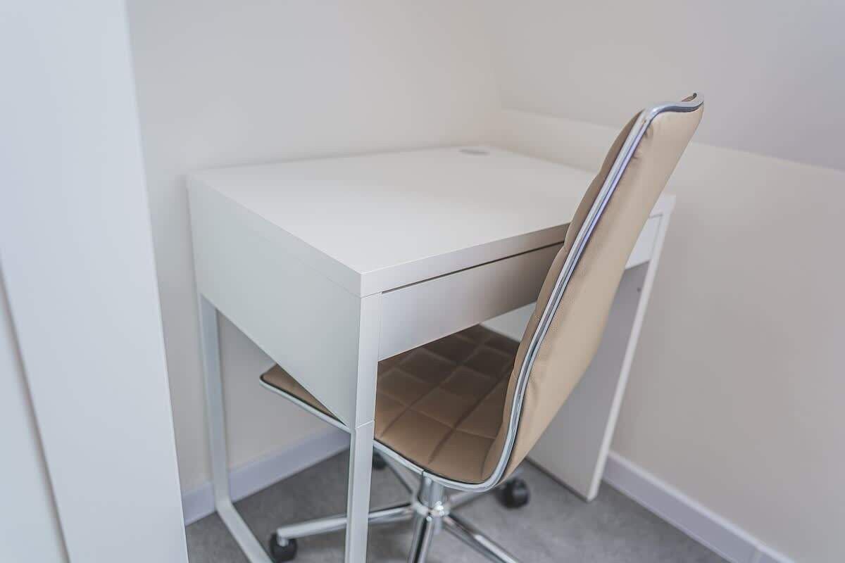 A white desk with a chair that has a cushioned seat and a metal frame.