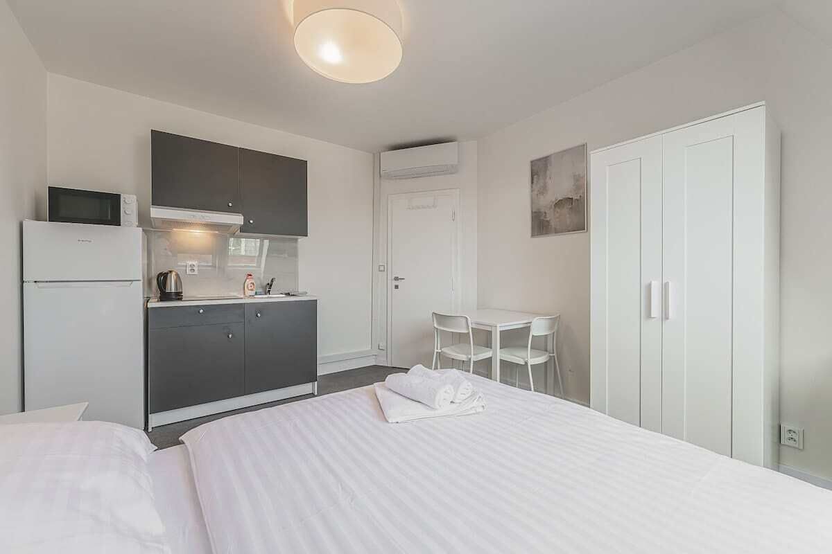 Quarto de hotel com cama, cozinha compacta, área de refeições e guarda-roupa.