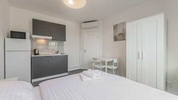 Quarto de hotel com cama, cozinha compacta, área de refeições e guarda-roupa.