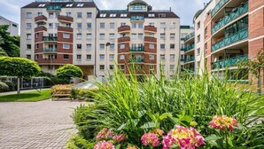 Um edifício residencial com vários andares, varandas, um pátio pavimentado e vegetação exuberante.