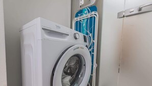 Máquina de lavar frontal numa lavanderia com um porta-roupas azul e uma porta branca.