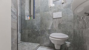 Et badeværelse med toilet, bruseområde og en lille hylde med toiletartikler.
