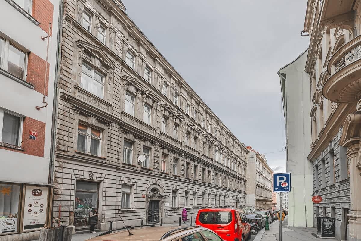 A historic building with classical architecture, a parking sign, and a red vehicle parked on the street.