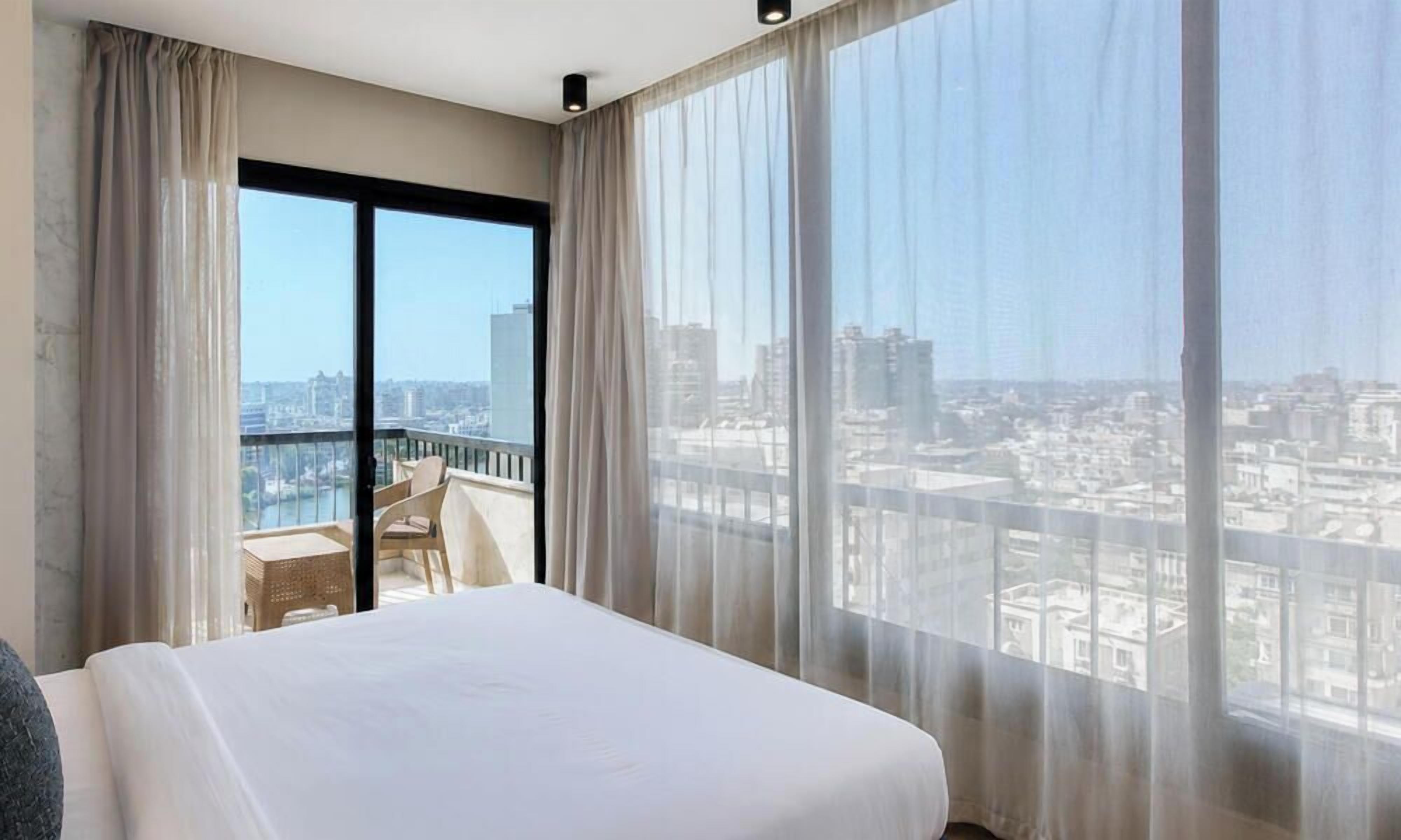 Una habitación de hotel con una cama grande, un balcón con vistas a la ciudad y cortinas de gasa.
