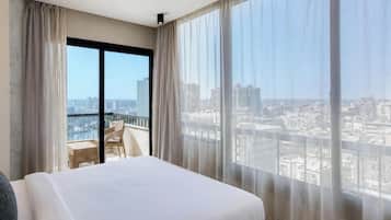 A hotel room with a large bed, a balcony with a view of the city, and sheer curtains.
