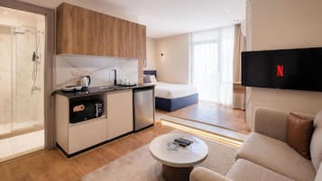 A modern hotel room with a kitchenette, a bed, a TV, and a seating area.