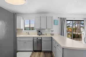 A modern kitchen with grey cabinets, a dishwasher, a coffee maker, and a window with blinds. - Beach House Hideaway Near Schooners, Sand & Grand Lagoon Fun (Panama City)