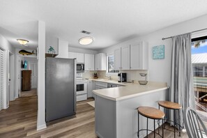 Une cuisine moderne avec des meubles blancs, un réfrigérateur gris, un îlot central doté de tabourets et une vue par la fenêtre.