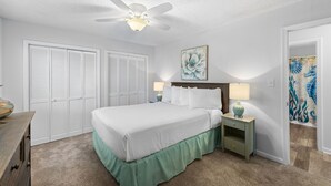 Ein Schlafzimmer mit einem Bett, zwei Nachttischen, einem Deckenventilator und einer Tür mit einem dekorativen Gemälde.