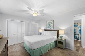 A bedroom with a bed, two bedside tables, a ceiling fan, and a door with a decorative painting. - Beach House Hideaway Near Schooners, Sand & Grand Lagoon Fun (Panama City)