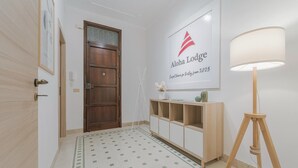 Um corredor com uma porta de madeira, um armário branco com um logotipo, uma luminária e um tapete estampado.