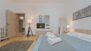 Quarto de hotel com uma cama, uma escrivaninha com computador, televisão e uma obra de arte com tema de zebra na parede.