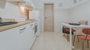 Uma cozinha compacta com armários brancos, bancada de madeira, forno embutido e um espaço de refeições com mesa e cadeiras.