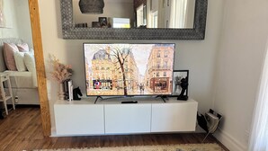 A living room with a television, a large mirror, a blue tufted ottoman, a white console, and a patterned rug. - Luxurious comfort & cosy, your home away from home! Romantic getaway… (Moyhu)