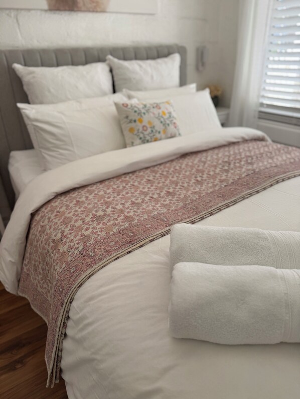 A neatly made bed with a patterned throw, a grey upholstered headboard, and white bedding.