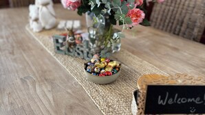 A wooden table with a woven placemat, a bowl of colorful candies, a vase of pink roses, a white bunny figurine, and a 'Welcome' sign. - Luxurious comfort & cosy, your home away from home! Romantic getaway… (Moyhu)