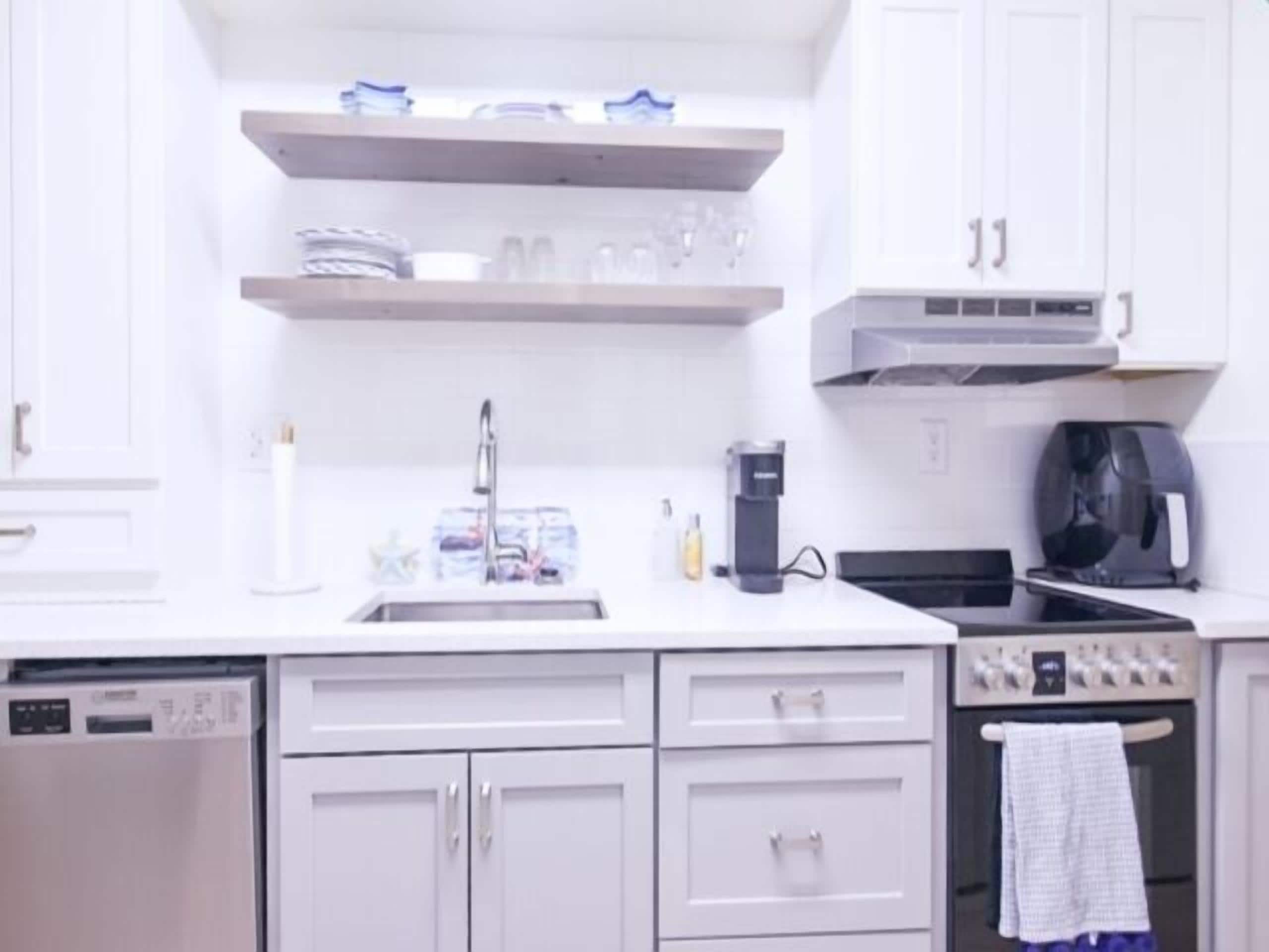 A kitchen with white cabinets, a sink, a coffee maker, and a stove.
