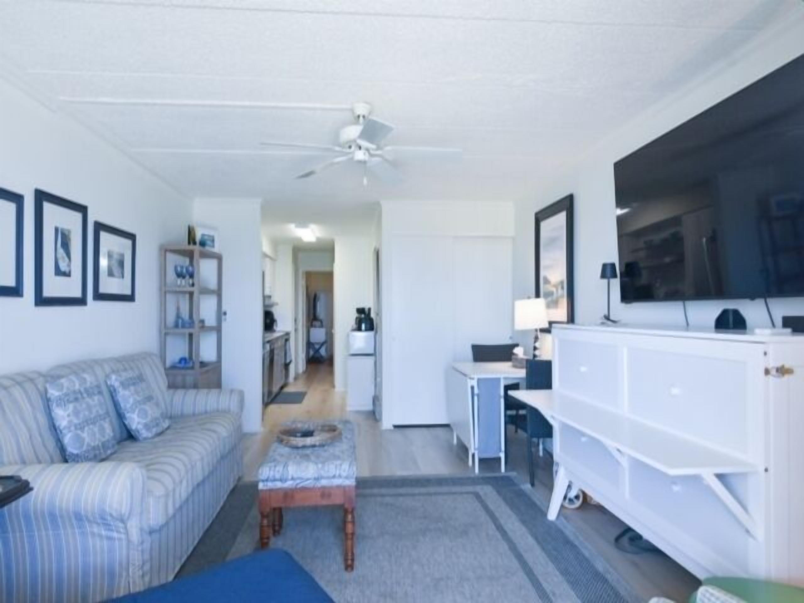 A living room with a sofa, a coffee table, a television, and a ceiling fan.