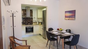 A dining area with a table set for four, a kitchen in the background, a coat rack, and a painting on the wall. - Spacious apartamens nearthe mall (Pafos)