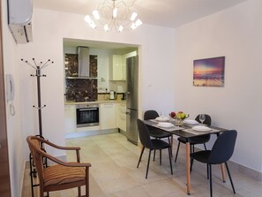 A dining area with a table set for four, a kitchen in the background, a coat rack, and a painting on the wall. - Spacious apartamens nearthe mall (Pafos)