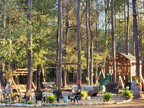 A forested area with a wooden cabin, a swing set, and outdoor seating. - Cozy 1 bedroom on 13 acres (Cleveland)
