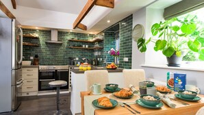 A modern kitchen with green tiles, a dining area with a wooden table, and a large window with a plant. - Wonderful  villa for 6 people with WIFI (Porthleven)