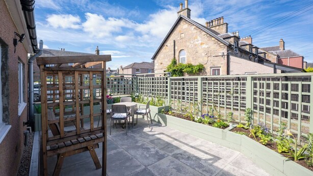 A patio with a wooden easel, outdoor seating, and a garden bed with plants. - Beautiful  villa for 5 people with WIFI, TV and patio (Inverness)