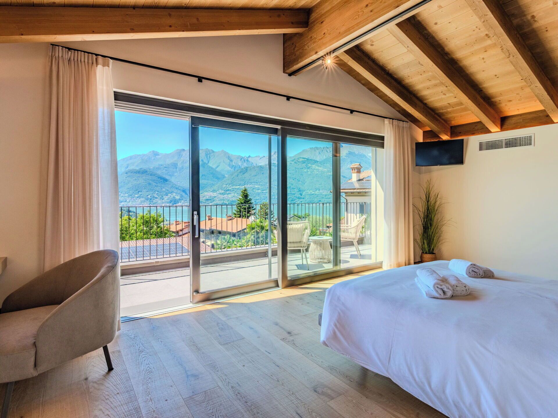 A bedroom with a large bed, a chair, and a balcony with a mountain view.