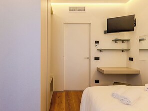 Ein Hotelzimmer mit einem Bett, einem an der Wand befestigten Fernseher, einem Wandregal und einer Tür.