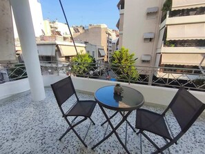 A balcony with a round table and two chairs, a small potted plant, and a view of surrounding buildings. - Center Hub (Dafni)
