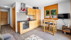 A compact kitchen with wooden cabinets, a stove, and a dining area with two chairs. - Sandra's Farm F0 - Cozy with a Terrace, in the Center (Haute-Nendaz)