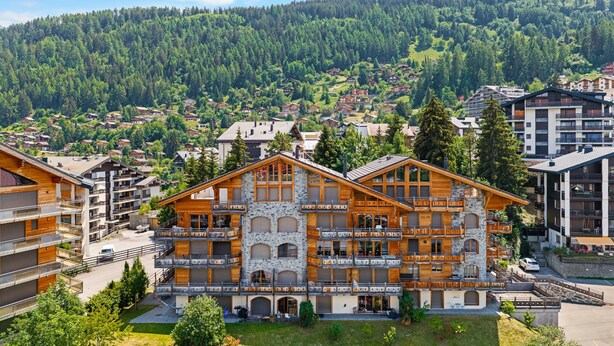 A multi-story hotel with balconies, a stone facade, and a view of a forested mountain. - Sandra's Farm F0 - Cozy with a Terrace, in the Center (Haute-Nendaz)